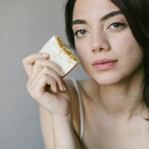 Woman holding natural soap bar near face, showcasing eco-friendly skincare in soft natural light.